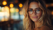 © samuel_miles - Young woman with glasses smiles warmly in a cozy café during golden hour