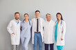© Studio Romantic - Group of young and adult doctors clinicians and cardiologists in scrubs and white coats standing together, hugging each other and smiling at camera on gray background. Happy clinic or hospital staff.