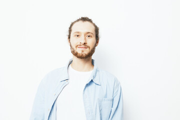 Smiling young man with a beard in casual denim shirt stands against a white background, radiating confidence and positivity, ideal for lifestyle and wellness themes