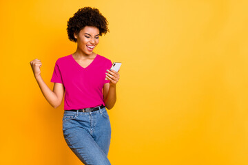 Wall Mural - Copyspace photo of fashionable stylish trendy cheerful champion curly wavy having received feedback looking at phone screen wearing jeans denim orange t-shirt isolated yellow vivid color background