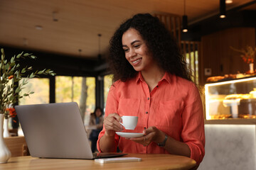 Woman with cup of coffee working on laptop in cafe