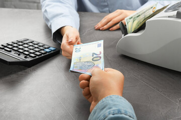 Wall Mural - Client giving euro banknotes to cashier at table in money exchange, closeup