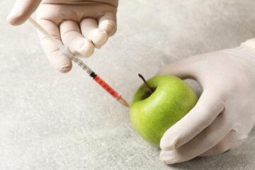 Wall Mural - gmo concept. scientist injecting something into green apple at grey table, closeup