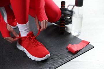 Wall Mural - Woman tying shoelaces and gym equipment indoors, closeup