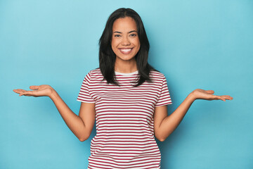 Wall Mural - Filipina young woman on blue studio makes scale with arms, feels happy and confident.