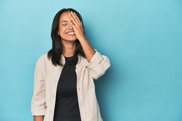 Wall Mural - Filipina young woman on blue studio laughing happy, carefree, natural emotion.