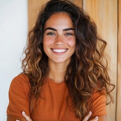 Wall Mural - A young woman with long, curly brown hair smiles warmly while wearing a burnt orange t-shirt.