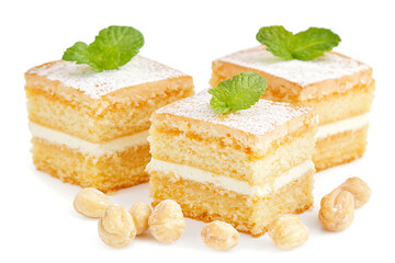 Wall Mural - Three layered sponge cakes dusted with powdered sugar and topped with mint surrounded by hazelnuts on a white background.