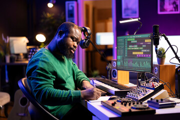 Fototapete - Talented artist composing new lyrics for his tracks and recording music with audio devices in his home studio. Singer composer writes melodic material by taking notes and creating rhymes or songs.