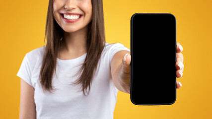 Wall Mural - Mobile Application Ad. Portrait Of Happy Lady Showing Smart Phone Black Empty Screen Recommending App Standing Over Yellow Orange Studio Background. Selective Focus On Cell Display, Check This Website