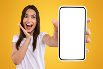 Wall Mural - Wow, Amazing Useful App. Portrait of excited and surprised young woman holding smartphone with black blank screen in hand, showing device, closeup. Gadget with empty free space for mock up template