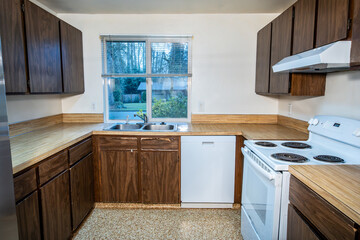 1970s vintage kitchen, dark brown cabinets, wood grain laminate counter tops, white walls and stainless steel sink, rental home interior damage after the tenant moves out, housing market
