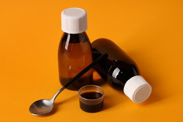 Wall Mural - Bottles and measuring cup of cough syrup with spoon on orange background