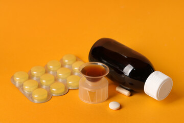 Wall Mural - Bottle and measuring cup of cough syrup with different pills on orange background