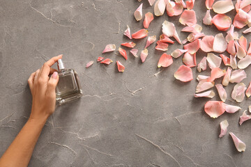 Wall Mural - Female hand with bottle of perfume and beautiful rose petals on grey grunge background