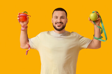 Wall Mural - Sporty young man with measuring tapes, bell pepper and fresh apple on yellow background. Healthy food concept