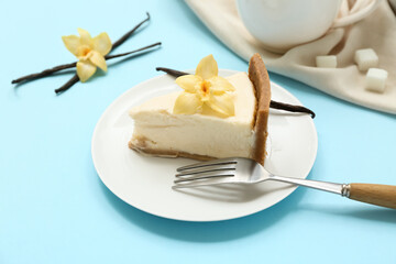 Wall Mural - Plate of sweet cheesecake slice with vanilla flowers and sticks on blue background