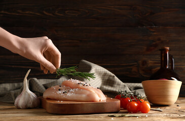 Wall Mural - Female hand with rosemary and raw chicken breast on wooden background