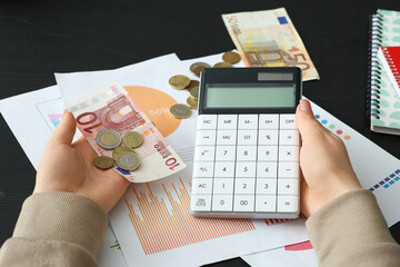 Wall Mural - Woman holding money with calculator and diagrams on dark table, closeup. Financial Wellness Month