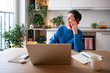 © DimaBerlin - Cheerful laughing mature woman chats on smartphone during study break at home. Adult student managing online courses on laptop, electronic learning, remote education, juggling tasks, home based work
