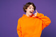 © ViDi Studio - Young shocked surprised happy Caucasian woman she wears orange hoody casual clothes doing phone gesture like says call me back isolated on plain purple background studio portrait. Lifestyle concept.