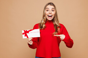 Poster - Young shocked surprised woman wear red casual clothes hold point finger on gift certificate coupon voucher card for store isolated on plain pastel beige background studio portrait. Lifestyle concept.