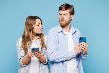 Wall Mural - Young couple two friends family man woman wear shirt casual clothes together hold in hand use look at mobile cell phone hiding screen isolated on plain light blue background studio. Lifestyle concept.