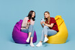 © ViDi Studio - Full body young couple two friends women wearing red casual clothes together sit in bag chair hold in hand use show mobile cell phone isolated on pastel plain light blue background. Lifestyle concept.
