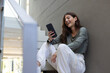 © Wavebreak Media - Sitting on stairs, woman holding smartphone and smiling, enjoying video call