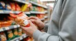 © Tati - Person in hoodie holding and examining snack bag supermarket aisle