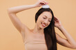 © anatoliycherkas - Smiling brunette woman massaging her head with a scalp brush on beige background