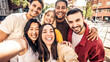 © Davide Angelini - Multicultural cheerful friends taking selfie pic with smart mobile phone device - Youth community people laughing at camera together - Friendship concept with guys and girls having fun outdoors