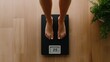 © anyatachka95 - Female measuring weight on digital scale on wooden floor with green plant nearby