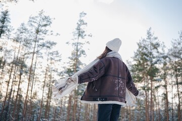 Young woman walking in forest among snow covered pines in winter day.