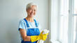 © Ольга Симонова - Portrait adult Asian Woman in blue apron and yellow rubber gloves with rag in his hand by window against a white wall, window cleaning service, house cleaning.