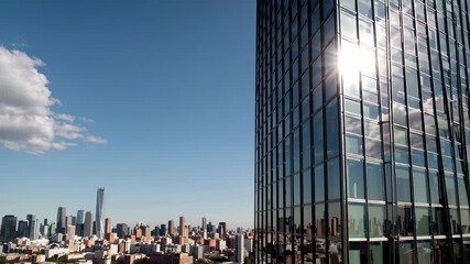 Poster - Sunlight reflects on the glass facade of a modern skyscraper in a bustling metropolis, creating a dynamic interplay of light and shadow in slow motion