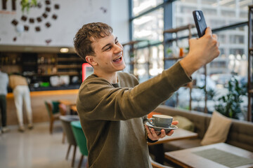 Wall Mural - young man show cup of coffee while have video call on cellphone