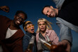 © liderina - Group of Multi-Ethnicity people having fun outdoor in the night. Celebrate. Low angle view.