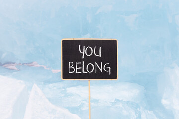 Wall Mural - Belonging and you belong symbol. Concept words You belong on beautiful yellow chalk blackboard. Beautiful Baikal lake blue ice background. Business belonging and you belong concept. Copy space.