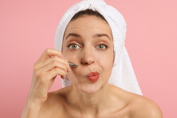 Canvas Print - Beautiful woman plucking her facial hair with tweezers on pink background