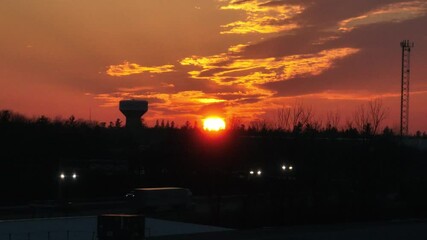 Wall Mural - Orange sunset view with silhouetted trees and water tower in the background of a busy street