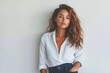 © Anjali - A young woman with wavy brown hair and tanned skin poses confidently in a white shirt and jeans against a white background.