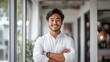 © Olena - Asian Man in a White Shirt with Crossed Arms Against a Modern Interior Background (Gestures, Emotions, Confidence)