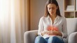 © Have a Good Day - Caucasian woman in a bright living room suffering from stomach pain caused by menstrual cramps