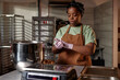 © Seventyfour - Waist up shot of concentrated Black female pastry chef rounding piece of raw dough into cookies at working station in bakery kitchen