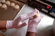 © Seventyfour - Close up on hands of Black female baker working in vinyl gloves rolling piece of dough to make round wheat buns in commercial kitchen, copy space