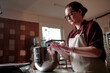© Seventyfour - Low angle shot of young female baker wearing apron and vinyl gloves rounding piece of dough forming biscuits while baking pastries in commercial kitchen