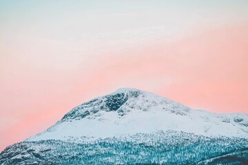 Sunset casts a glow on a snowcapped mountain amidst clouds