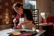© Seventyfour - Medium shot of young female confectionary chef enjoying process of assembling delicious cake spreading cherry jam over moist layer with knife, while working at table in patisserie kitchen