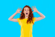 © Iryna - Excited young woman with curly hair poses in bright yellow shirt against blue background